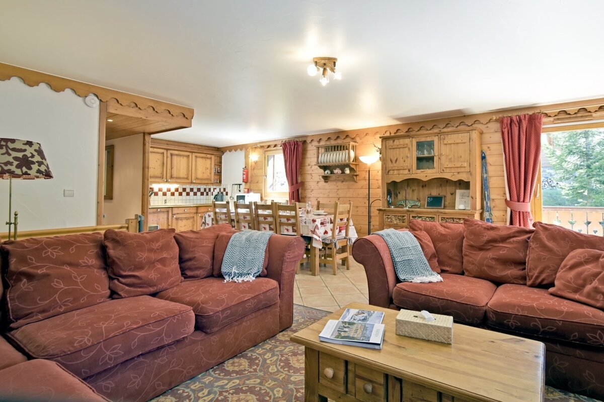 Cozy chalet interior with red patterned sofas, a wooden coffee table, and a dining area in the background.