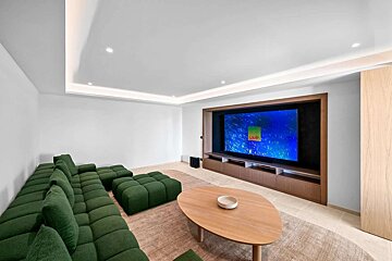 A modern media room featuring a large green modular sofa, a unique wooden coffee table, and a big TV screen built into a sleek wooden unit.
