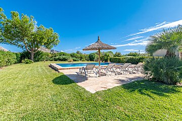 A lawn with a swimming pool and chairs under an umbrella