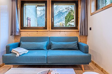 A blue couch sits in front of a window with mountains in the background