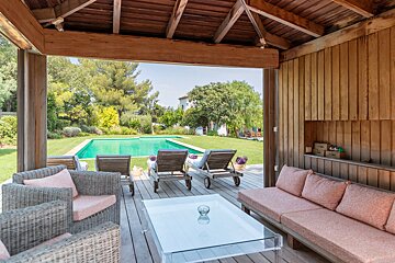 A wooden gazebo with a swimming pool in the background