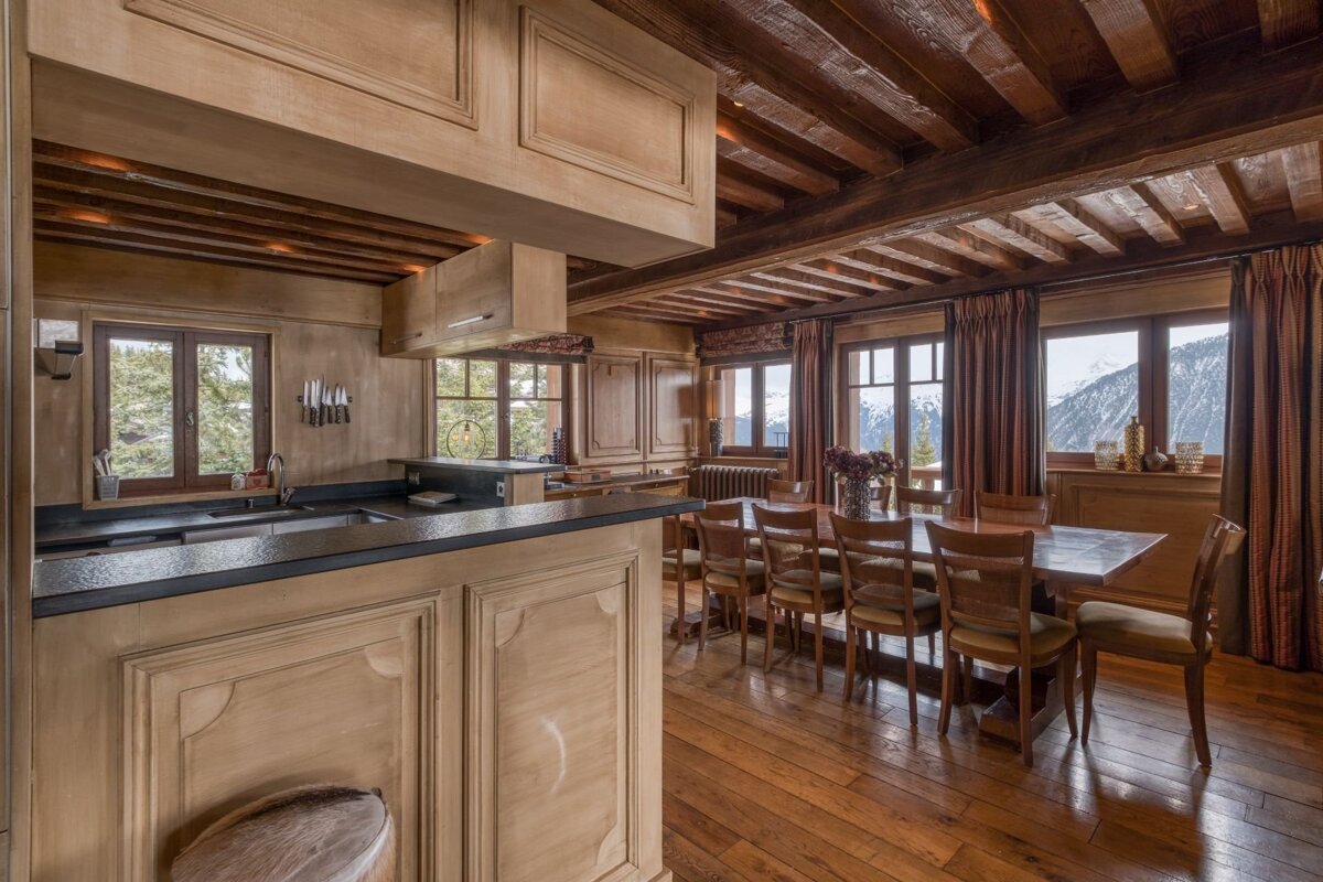 Cozy, rustic kitchen and dining room with wooden interiors, beamed ceilings, and scenic mountain views from wide windows.