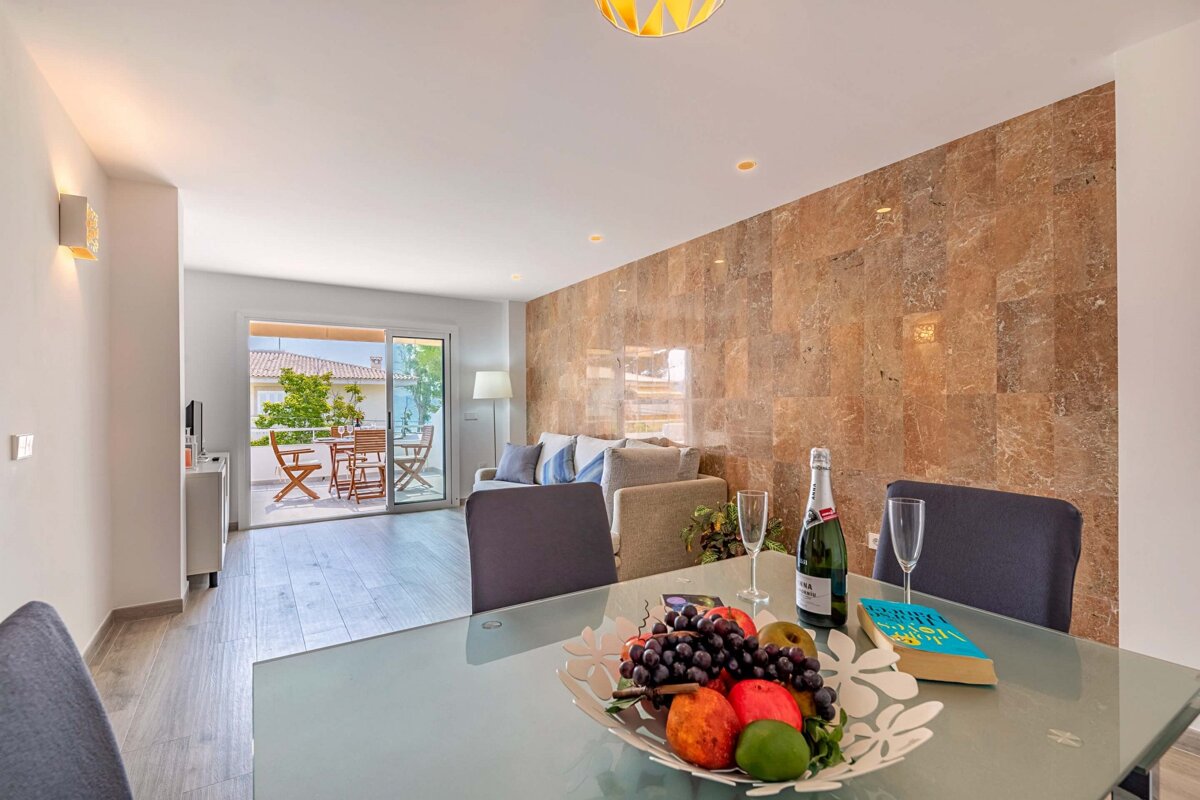 A bowl of fruit sits on a dining table next to a bottle of champagne