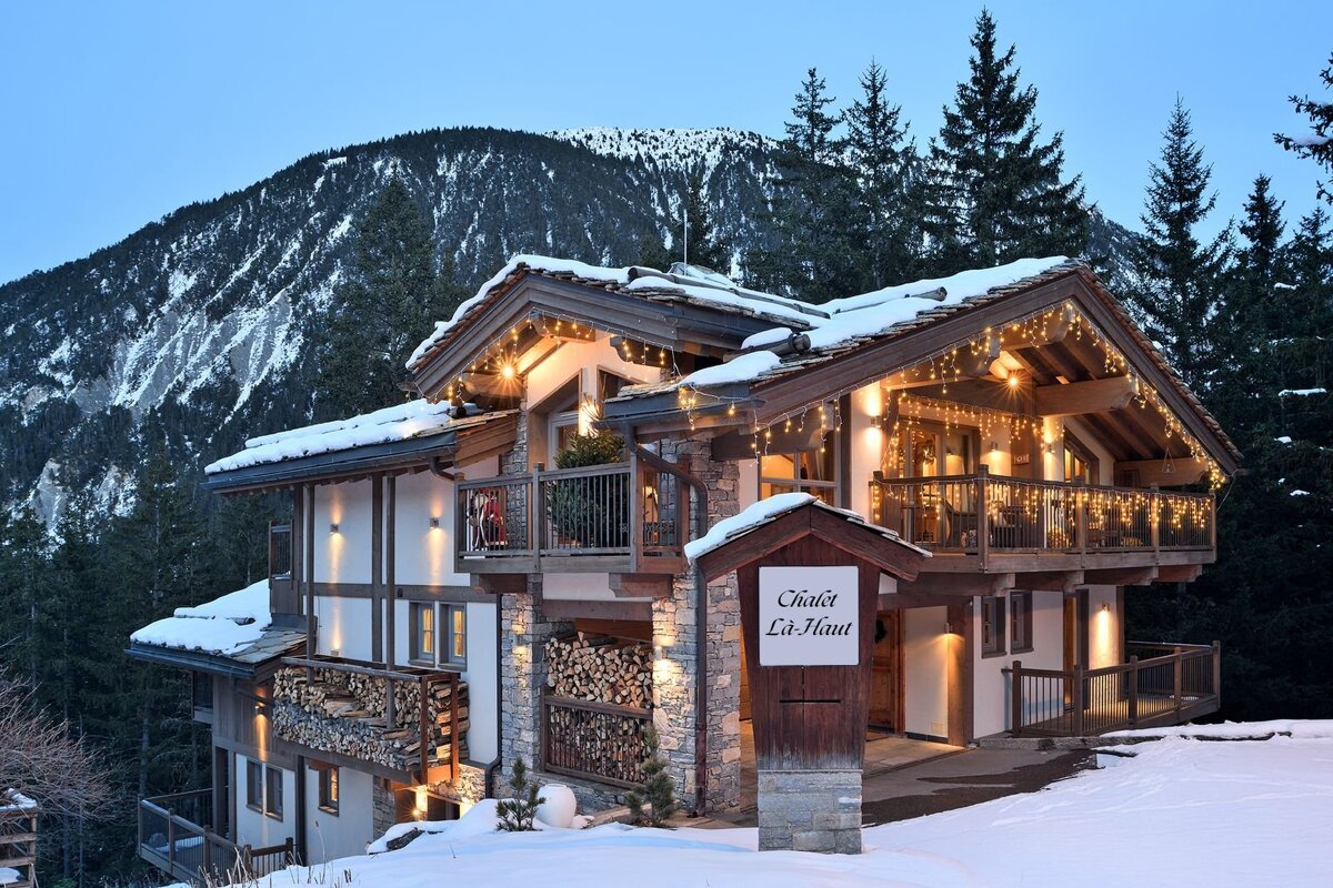 Cozy snow-covered mountain chalet "Chalet L&agrave;-Haut" glowing with warm lights in a scenic winter alpine landscape.