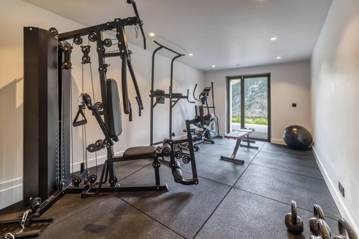 Modern home gym with a multi-gym machine, bench, exercise ball, and weights on rubber tile flooring.