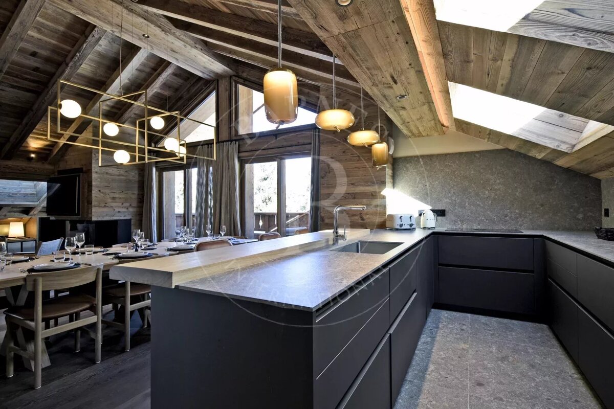 Modern chalet kitchen and dining area featuring dark cabinetry, stone countertops, wooden ceilings, and contemporary lighting.