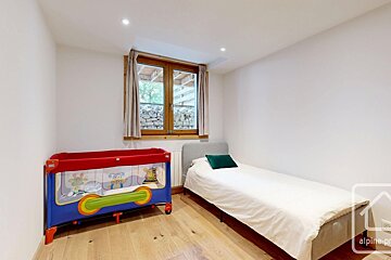 A simple bedroom containing a single bed and a colorful baby cot, next to a window.