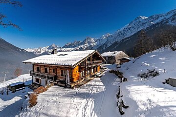 Rustic wooden chalets covered in snow, nestled amidst majestic snow-capped mountains under a clear blue sky on a bright winter day.