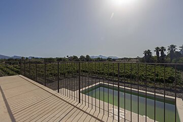 Sunny balcony view over a green vineyard, distant mountains, and a small green pool under a bright blue sky.
