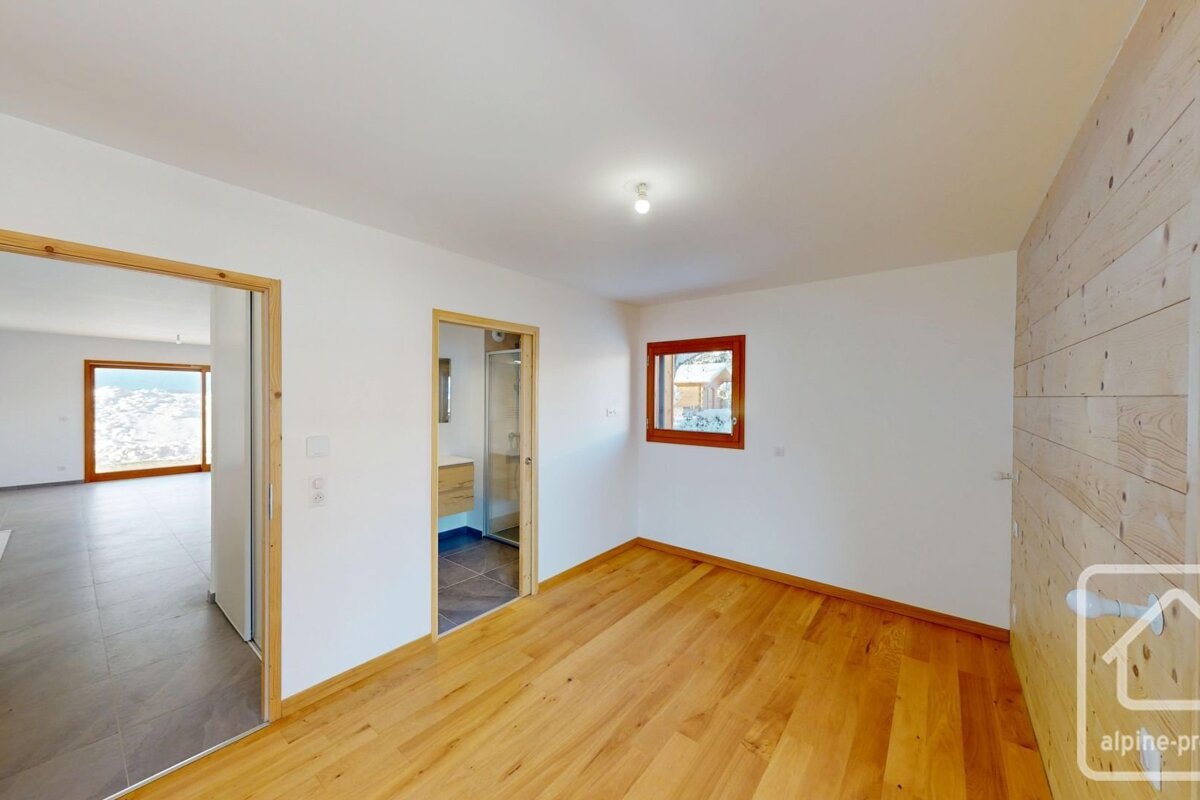 Bright room with wooden floor, white walls, and a wood-paneled accent wall. Features doors to a mountain-view room and a bathroom.