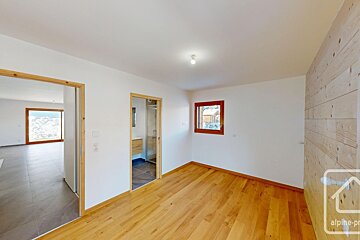 Bright room with wooden floor, white walls, and a wood-paneled accent wall. Features doors to a mountain-view room and a bathroom.