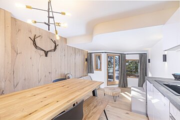 Modern apartment interior with a wood-paneled wall, large dining table, minimalist lighting, and a bright living area.