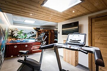 A cozy home wellness area featuring a treadmill, exercise bike, hot tub, and a sauna under a rustic wooden ceiling.