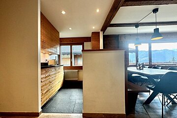 A chalet interior with a rustic wooden kitchen and an adjacent dining area featuring mountain views.