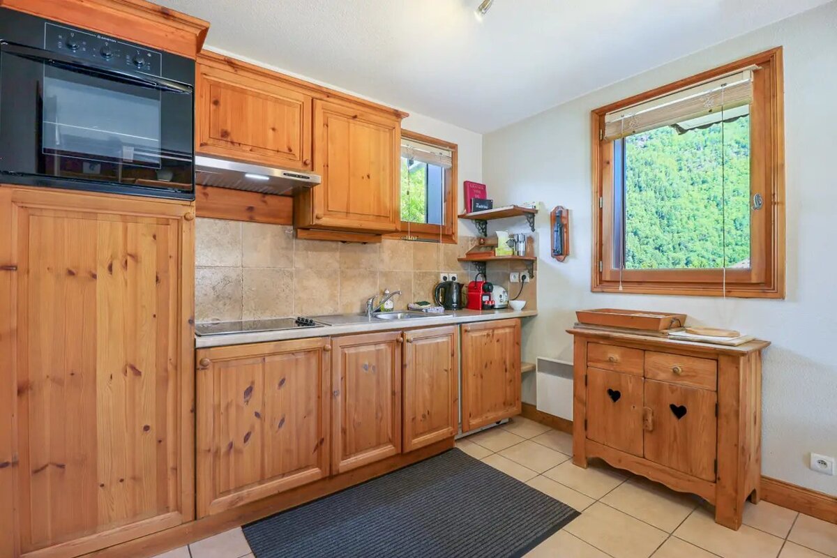 Cozy rustic kitchen featuring warm pine wood cabinets, a built-in oven, and a window overlooking a lush green forest.