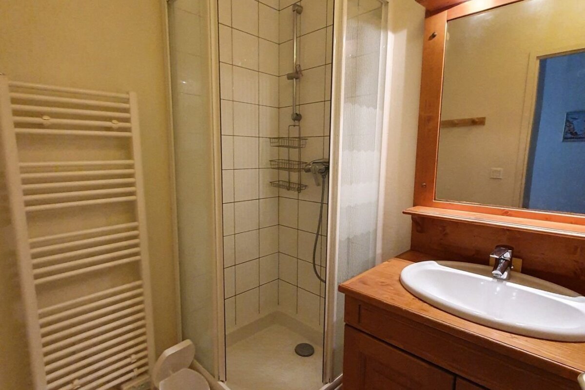 A cozy bathroom featuring a corner shower, a white heated towel rack, and a wooden vanity with a sink and mirror.