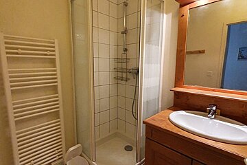 A cozy bathroom featuring a corner shower, a white heated towel rack, and a wooden vanity with a sink and mirror.