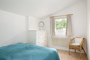 A bedroom with a blue blanket and a wicker chair