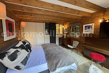 Cozy wooden-paneled room with a bed, artistic decor, piano, and windows, creating a warm, rustic ambiance.