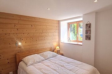 A cozy bedroom with a wooden paneled accent wall, a bed with white linens, a bedside lamp, and a bright window.