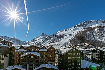 A sunny ski resort nestled in snow-covered mountains under a bright, clear blue sky.