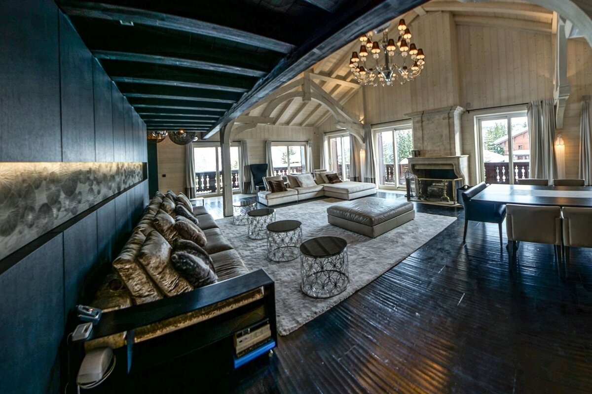 Luxurious chalet-style living and dining room with high vaulted ceilings, a grand fireplace, stylish seating, and large windows overlooking balconies.
