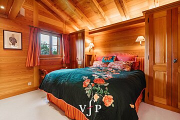 Cozy wood-paneled chalet bedroom featuring a bed with a dark floral quilt, warm lighting, and sloped ceiling.