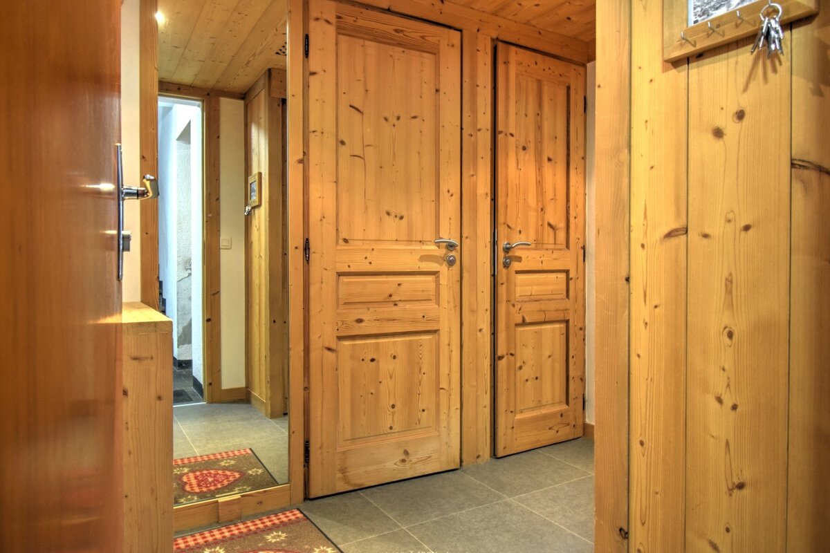 A rustic wooden hallway with multiple paneled doors, wood-paneled walls and ceiling, a tiled floor, a mirror, and keys hanging on the wall.