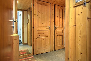 A rustic wooden hallway with multiple paneled doors, wood-paneled walls and ceiling, a tiled floor, a mirror, and keys hanging on the wall.