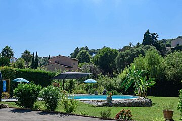 A large swimming pool is surrounded by a lush green garden