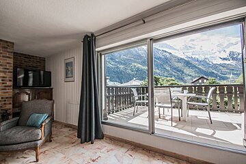 A living room with a balcony and mountains in the background