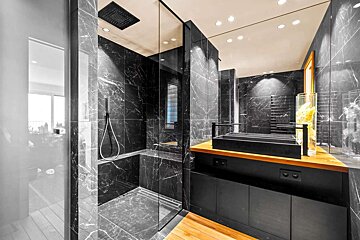 Sleek, modern bathroom with black marble walls and glass shower. Features a dark vanity on a wooden countertop, and recessed lighting on the ceiling.