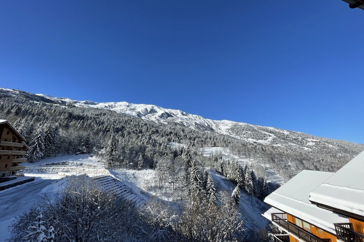 A breathtaking winter scene unfolds with snow-covered mountains, evergreen forests, and cozy chalets under a vibrant, clear blue sky.