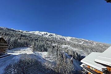 A breathtaking winter scene unfolds with snow-covered mountains, evergreen forests, and cozy chalets under a vibrant, clear blue sky.