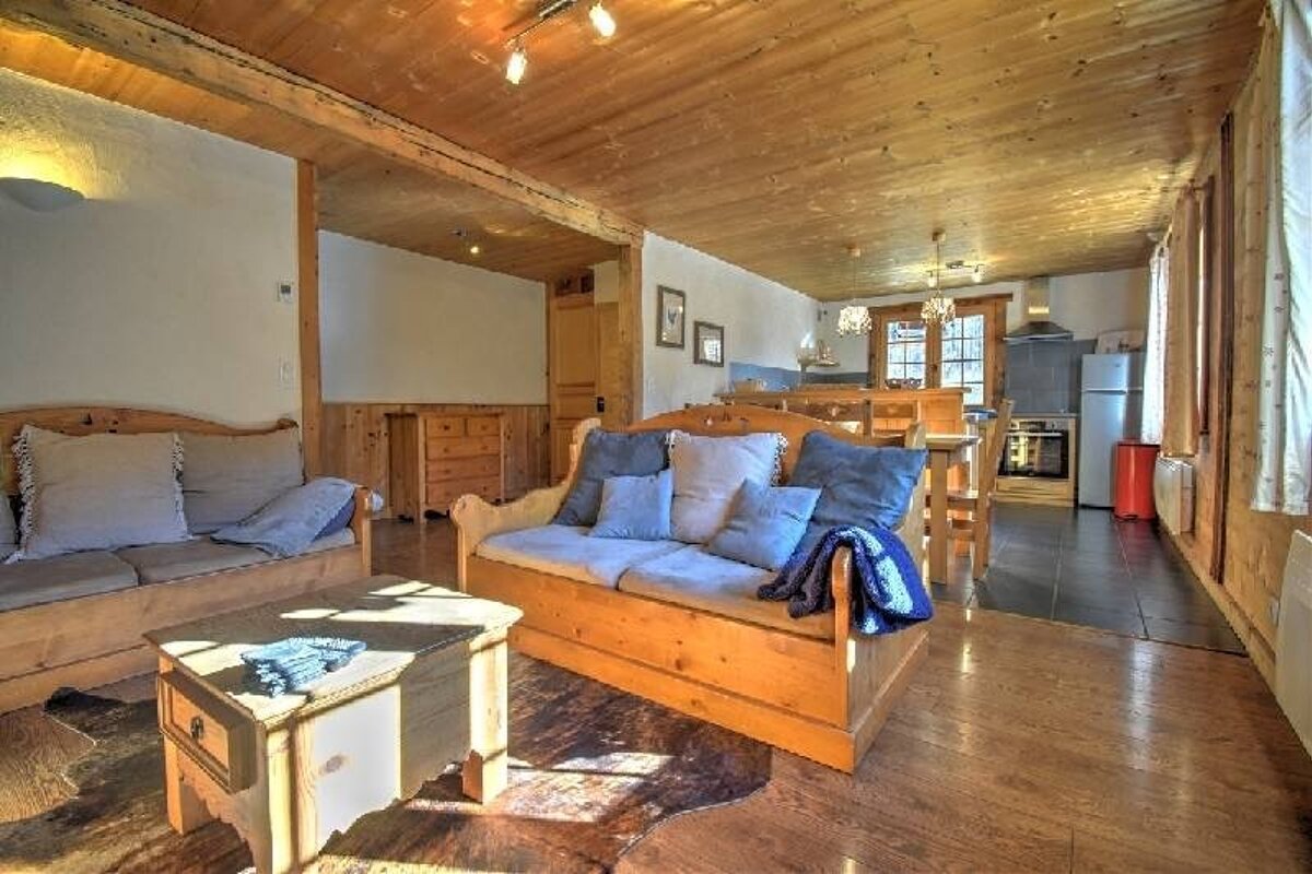 Cozy wooden cabin living room with two rustic sofas, a coffee table on a hide rug, and a kitchen visible in the background.