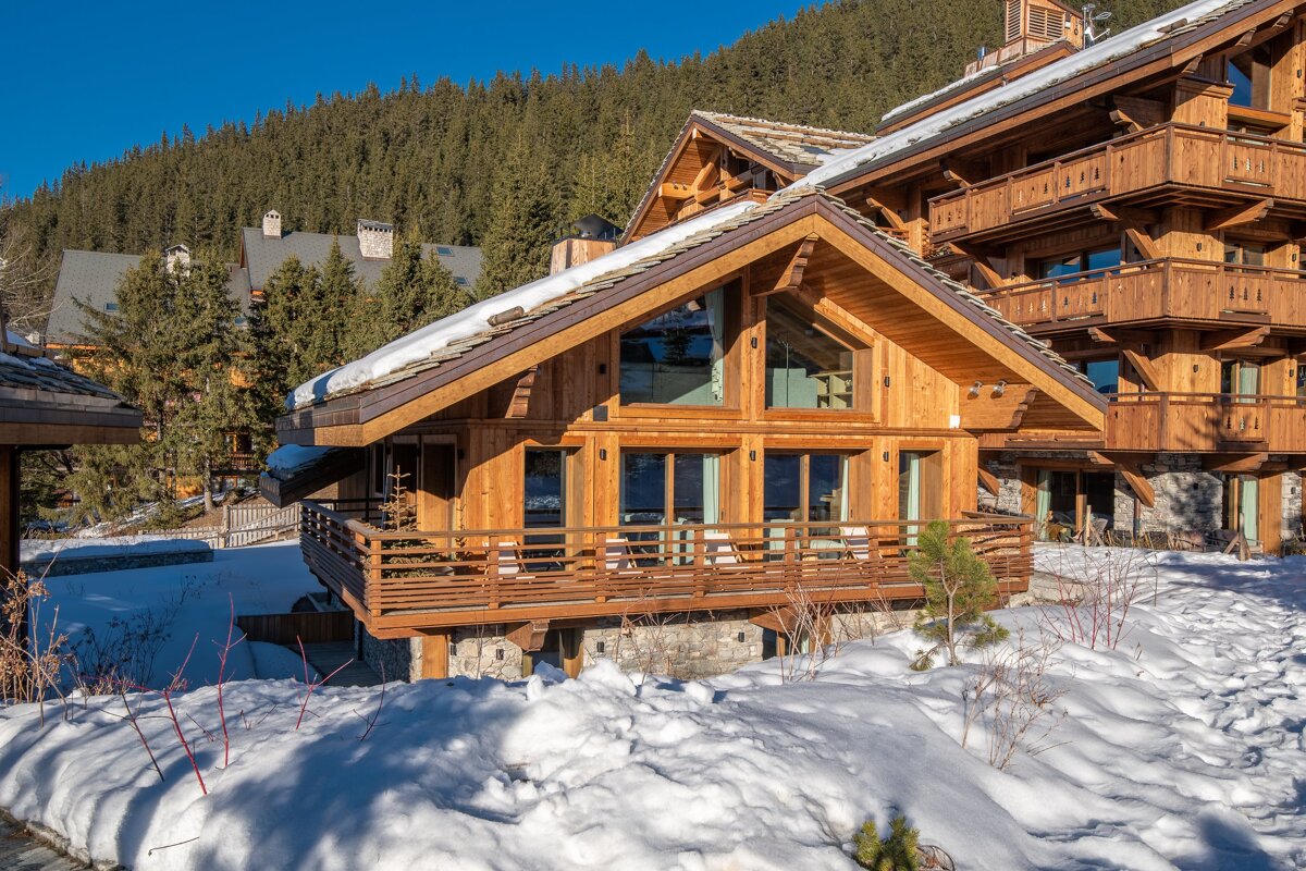 A large wooden house is surrounded by snow and trees