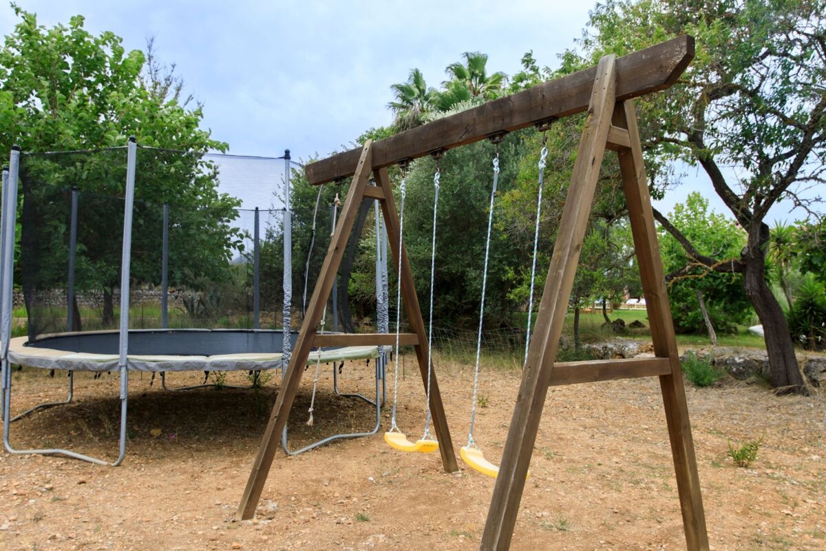A trampoline sits next to a wooden swing set