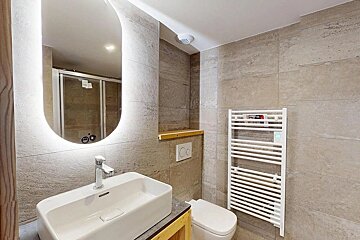Modern bathroom with a vessel sink, backlit mirror, beige tiled walls, wall-mounted toilet, and a white towel warmer.