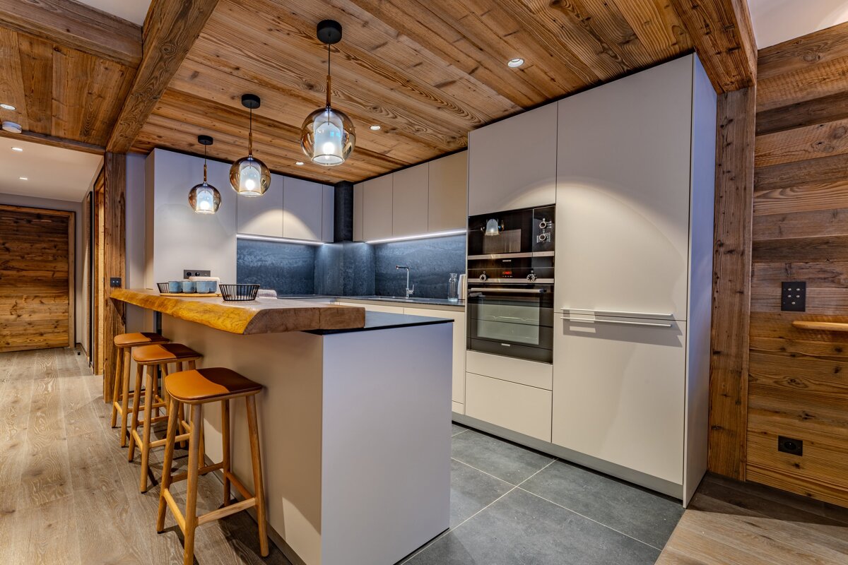 A chic modern kitchen with a large island bar, integrated appliances, and warm wooden ceilings and accents.