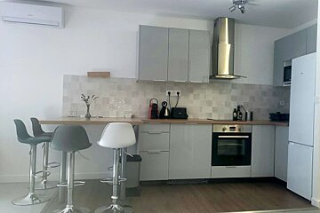Bright, modern kitchen with gray cabinets, wood bar counter, and three bar stools. Features oven, range hood, fridge, and air conditioning.