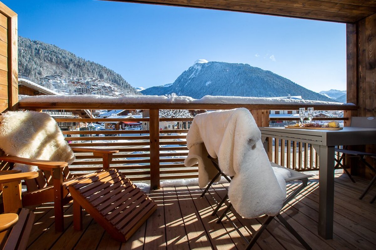 A balcony with chairs and a table with a mountain in the background