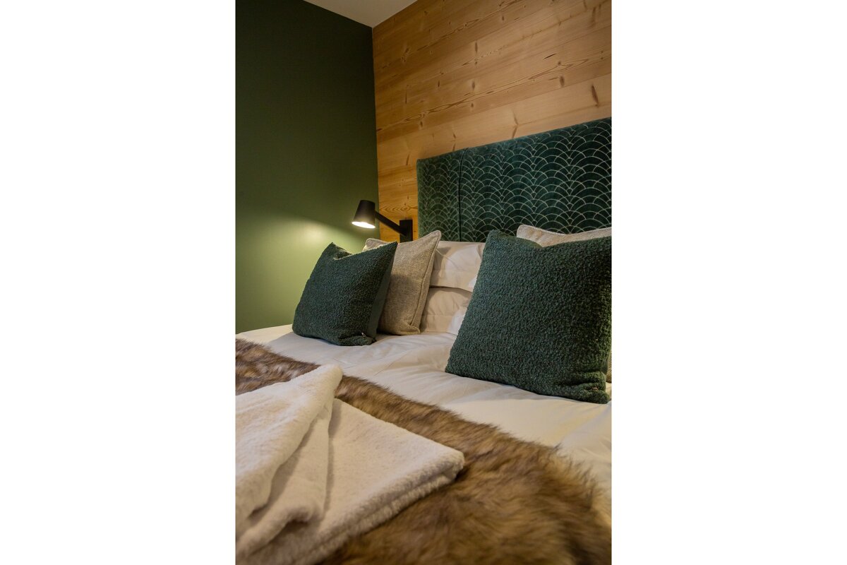 A bed with green pillows and a fur blanket