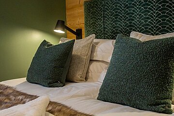 Cozy bed with textured green pillows, a patterned headboard, and a modern reading light casting a warm glow.