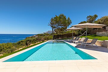 A large swimming pool surrounded by chairs and umbrellas overlooking the ocean