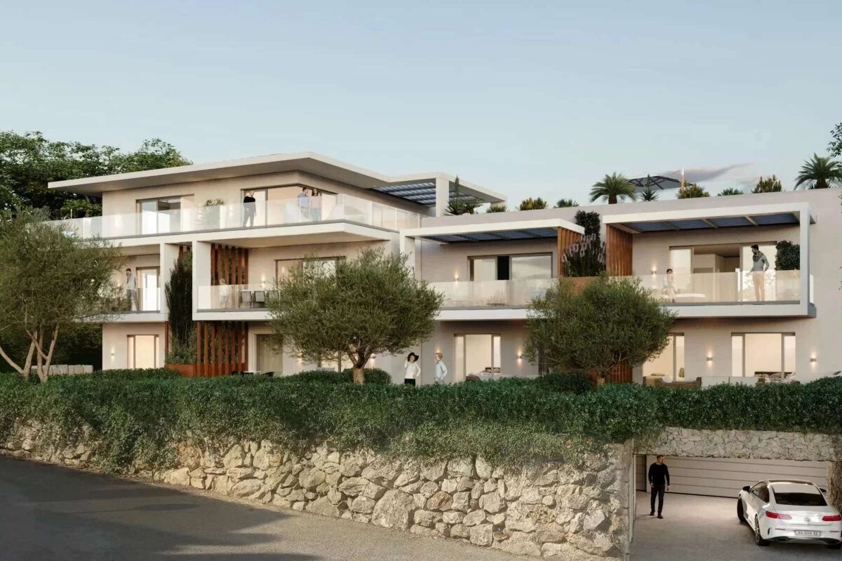 A modern, multi-story building with glass balconies and lush greenery sits above a stone wall. A white car is parked at an open garage with a person.