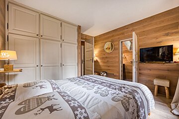 A rustic bedroom with light wood paneling, a large built-in wardrobe, a bed featuring reindeer and snowflake patterned bedding, and a mounted TV.