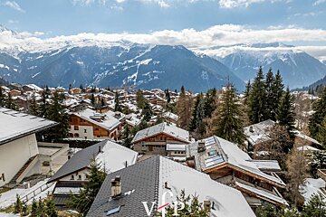 A snowy alpine village of chalets nestled below majestic, snow-capped mountains under a bright winter sky.