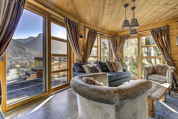 Cozy wooden chalet living room with large windows offering a scenic mountain view and comfortable seating.