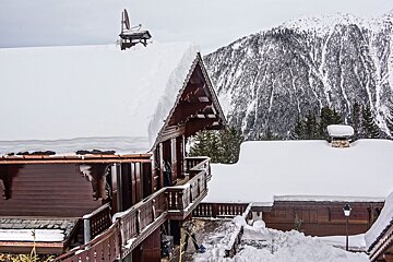 Heavily snow-covered wooden chalets with a vast, snowy mountain backdrop create a picturesque winter scene in the Alps.