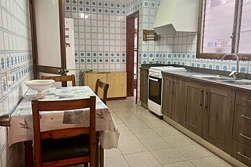 A retro-style kitchen with blue and white tiled walls, a dining table, brown cabinets, a stove, sink, and refrigerator.